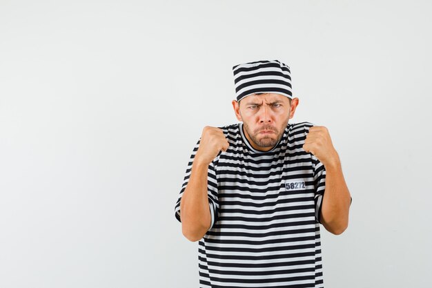 Young male keeping fists clenched in striped t-shirt hat and looking resolute  