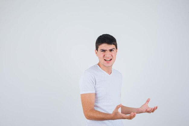 Young male keeping hands in aggressive manner in t-shirt and looking annoyed , front view.