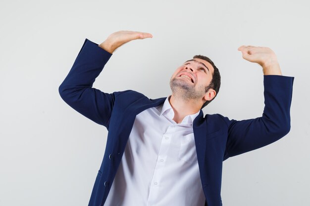 Young male keeping hands to defend himself in shirt and jacket and looking scared