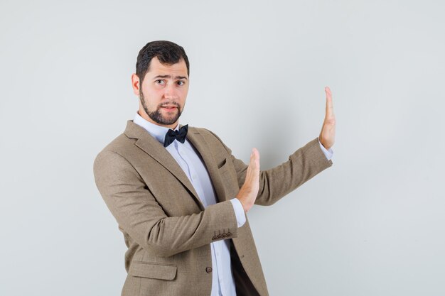 Young male keeping hands to defend himself in suit and looking uncomfortable. front view.