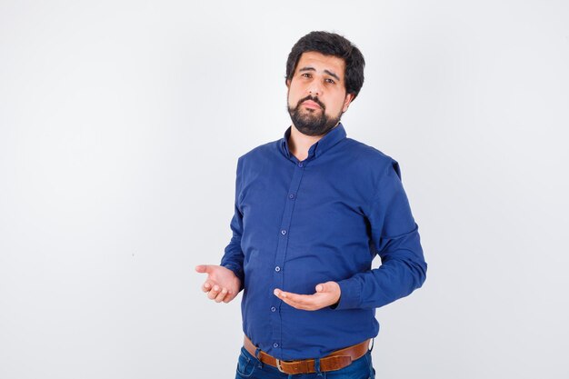 Young male keeping hands in praying gesture in blue shirt and looking innocent. front view.