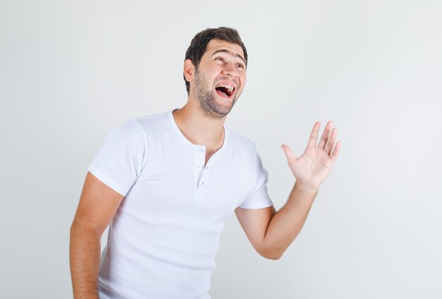 Young male laughing and keeping hand open in white t-shirt and looking happy
