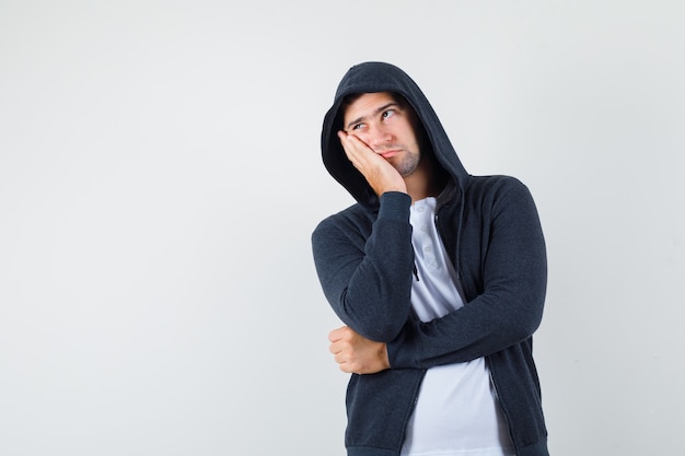 Free photo young male leaning cheek on palm in t-shirt, jacket and looking pensive. front view.