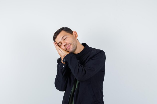 Young male leaning on palms as pillow in t-shirt, jacket and looking peaceful. front view.