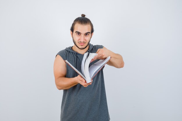 Молодой мужчина просматривает книгу в толстовке без рукавов и выглядит уверенно. передний план.
