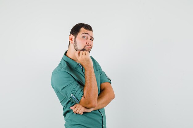 Young male looking aside in green shirt and looking interested , front view.