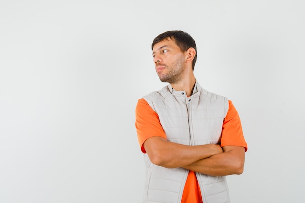 Young male looking aside with crossed arms in t-shirt, jacket and looking focused , front view.