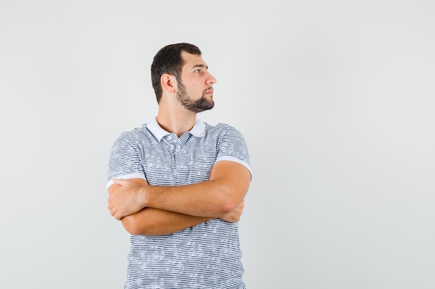 若い男性は、Tシャツを着て腕を組んで脇を見て、集中しているように見えます。正面図。