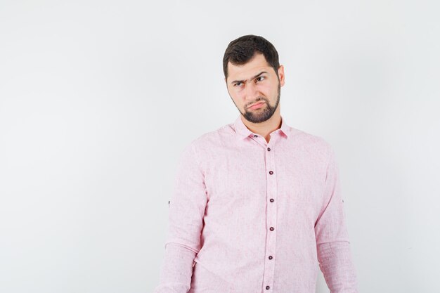 Young male looking away while scowling in pink shirt and looking gloomy