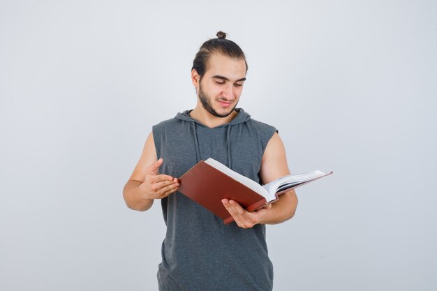 Молодой мужчина смотрит на книгу в толстовке без рукавов и смотрит сосредоточенным. передний план.