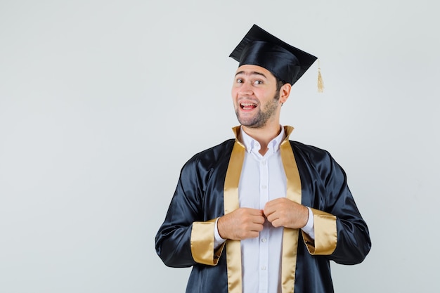 Free photo young male looking at camera in graduate uniform and looking cheerful , front view.