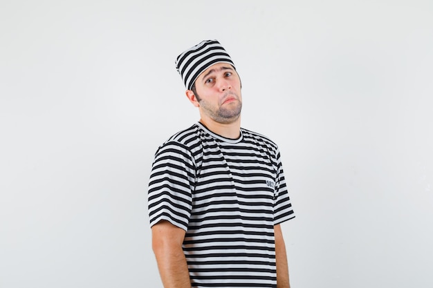 Young male looking at camera in t-shirt, hat and looking sad , front view.