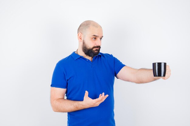 Young male looking at cup in blue shirt and looking sensible , front view.