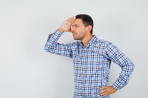Young male looking far away with hand over head in checked shirt and looking focused