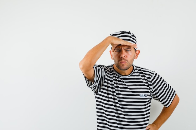 Young male looking far away with hand over head in striped t-shirt hat 