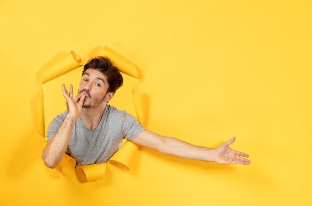 Young male looking from a torn yellow paper background facial guy sale indoor