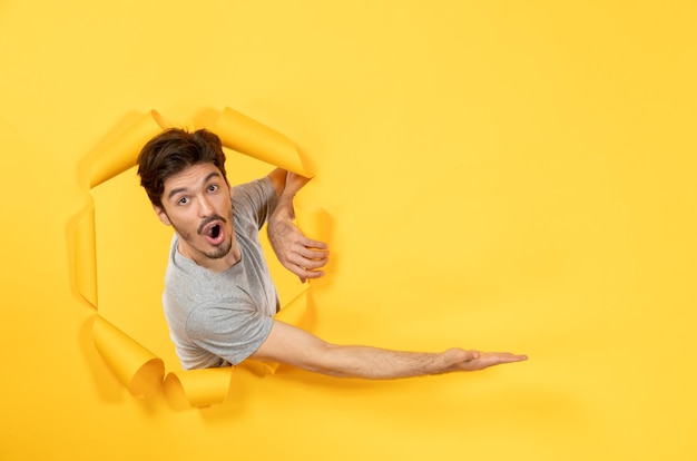 Young male looking from torn yellow paper background facial indoor guy