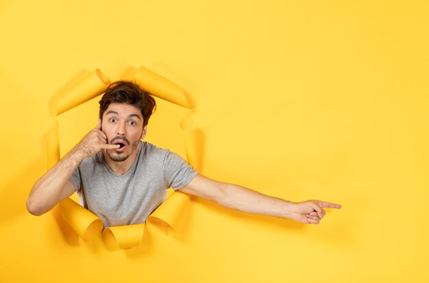 Young male looking from torn yellow paper background guy facial sale