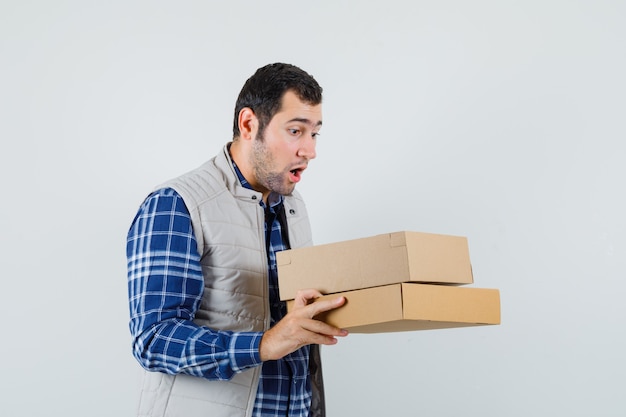 Young male looking into the box in shirt,jacket and looking surprised , front view.