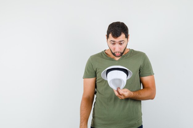 Young male looking into hat in green t-shirt and looking amazed