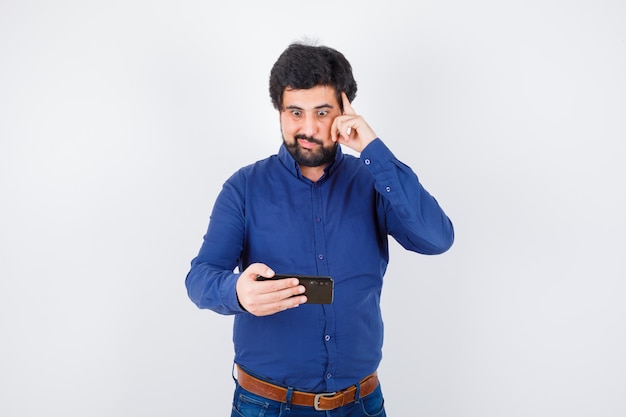 Young male looking at phone with hand on head in royal blue shirt and looking glad. front view.