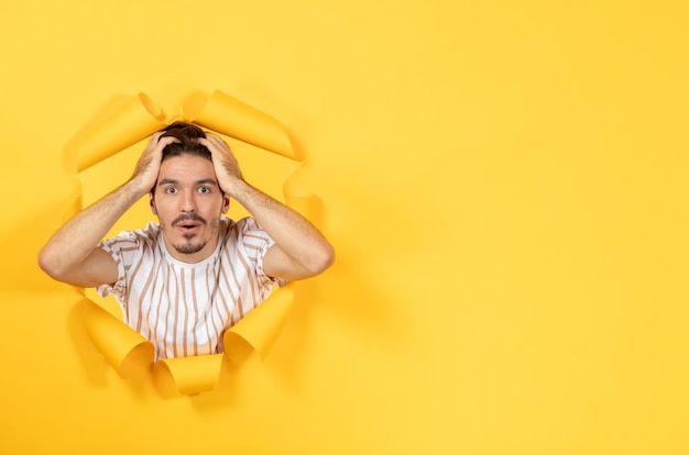 Free photo young male looking and standing on torn yellow paper background sale indoor facial guys