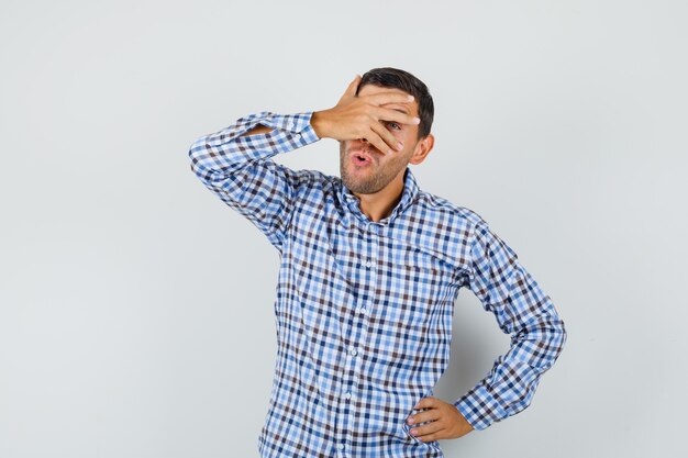 Young male looking through fingers in checked shirt and looking curious