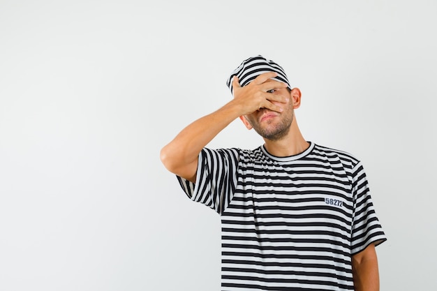 Young male looking through fingers in striped t-shirt hat and looking curious 