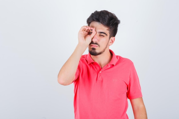 Young male looking through fingers in t-shirt and looking funny , front view.