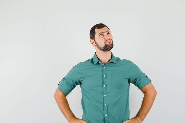 Young male looking up in green shirt and looking pensive , front view.