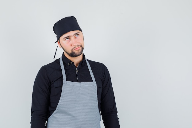 Young male looking up in shirt, apron and looking hesitant. front view.