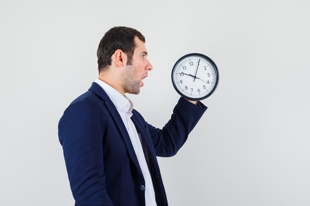 Young male looking at wall clock in shirt and jacket and looking surprised
