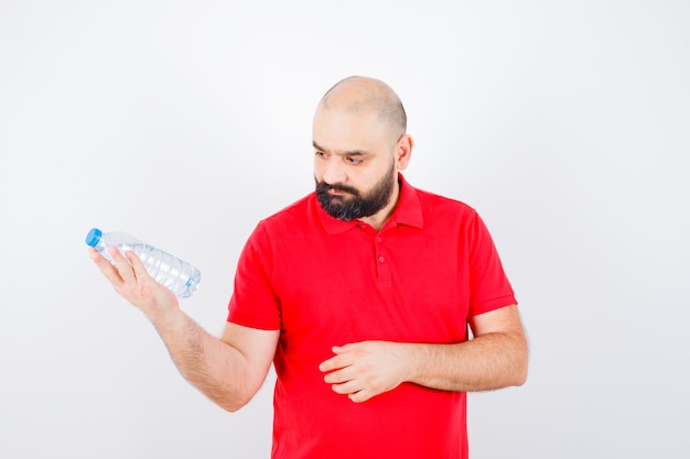 Young male looking at water bottle in red shirt front view.