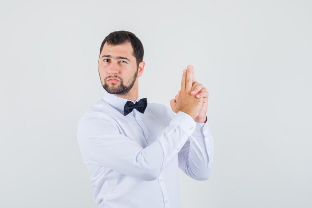 Young male making shooting gesture in white shirt and looking confident. front view.