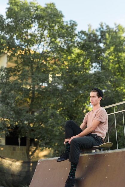 Free photo young male model sitting on skateboard