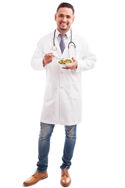 Молодой диетолог-мужчина ест здоровый салат и улыбается на белом фоне