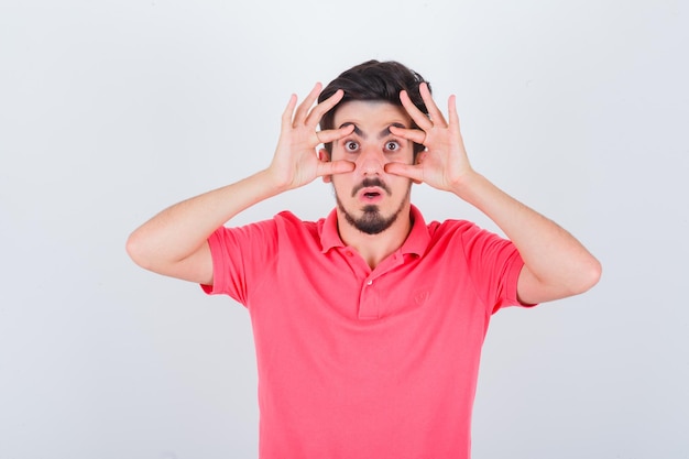 Young male opening eyes with hands in pink t-shirt and looking anxious. front view.