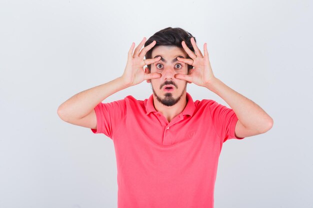 Young male opening eyes with hands in pink t-shirt and looking anxious. front view.