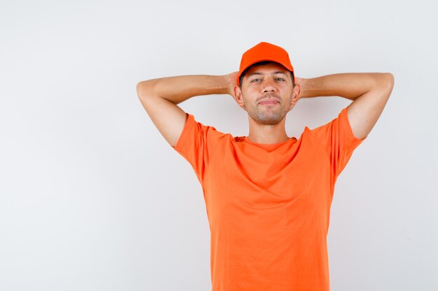 Young male in orange t-shirt and cap holding hands behind head and looking confident
