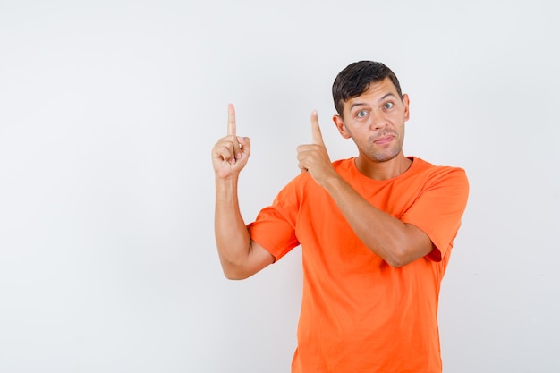オレンジ色のTシャツを着た若い男性が指を上に向けて注意深く見ている