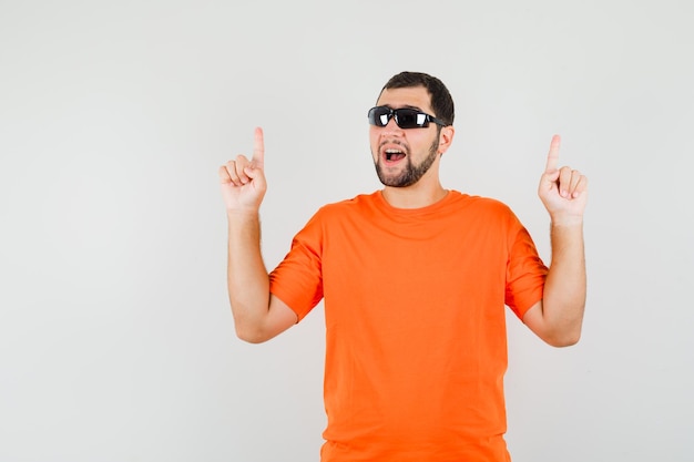 Young male in orange t-shirt pointing fingers up and looking confident , front view.