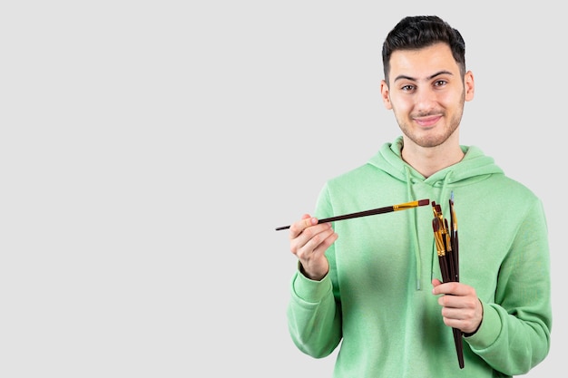 Free photo young male painter holding painting brushes over white