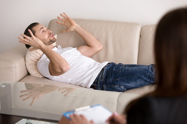 Young male patient lying on couch talking to female psychologist