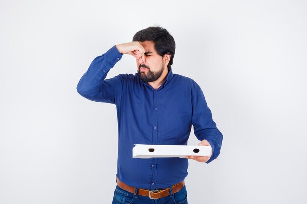 Free photo young male pinching nose due to bad smell in shirt, jeans and looking disgusted. front view.