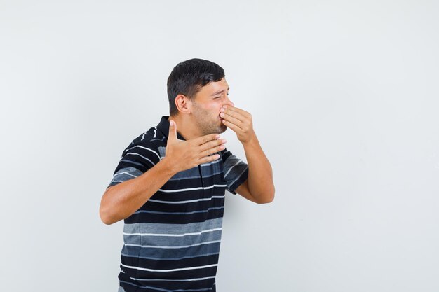 Young male pinching nose due to bad smell in t-shirt and looking disgusted. front view.