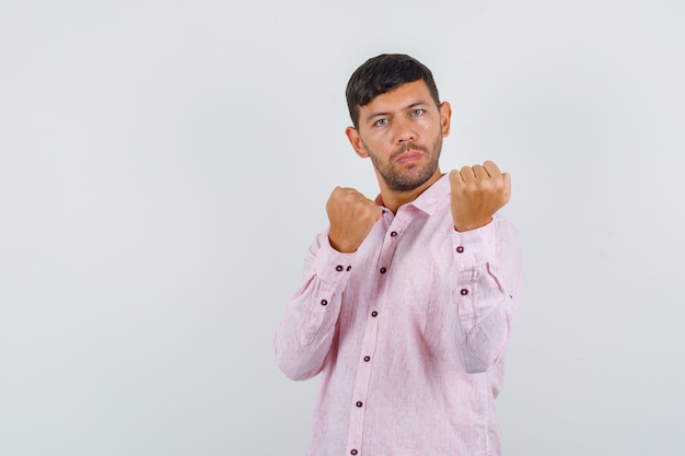 Young male in pink shirt holding fists in boxer pose and looking strong , front view.