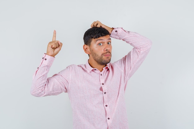 Free photo young male in pink shirt scratching head and pointing up , front view.