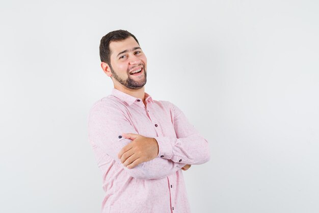 Young male in pink shirt standing with crossed arms and looking happy