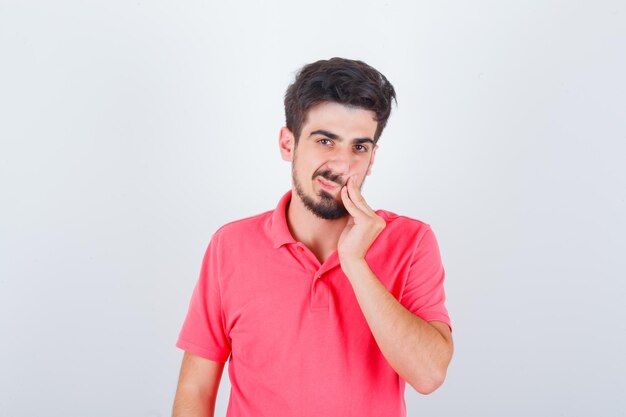 Молодой мужчина в розовой футболке с зубной болью и задумчивый вид спереди.