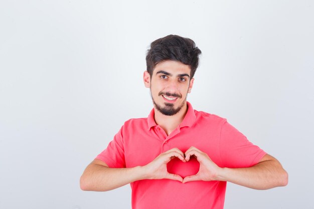 Young male in pink t-shirt showing heart gesture and looking confident , front view.